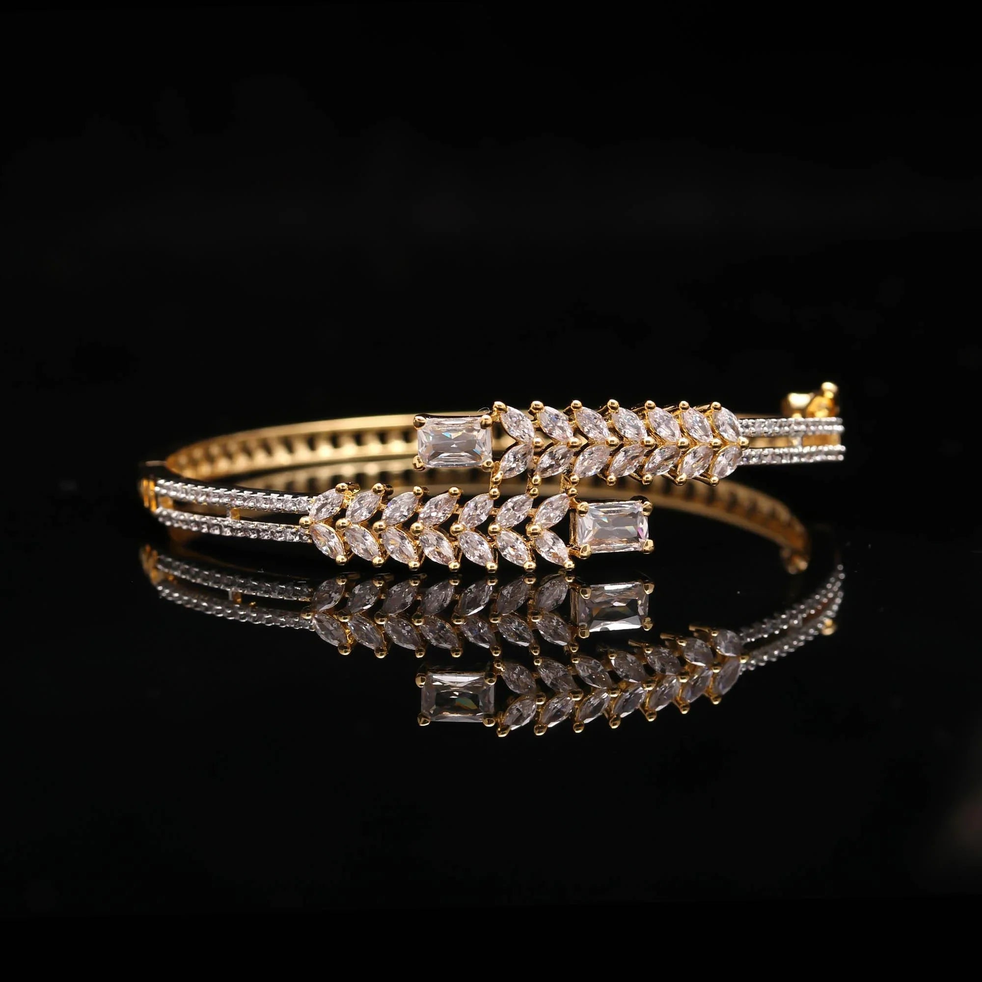 Elegant gold bracelet with clear rectangular and leaf-shaped crystals on black reflective surface