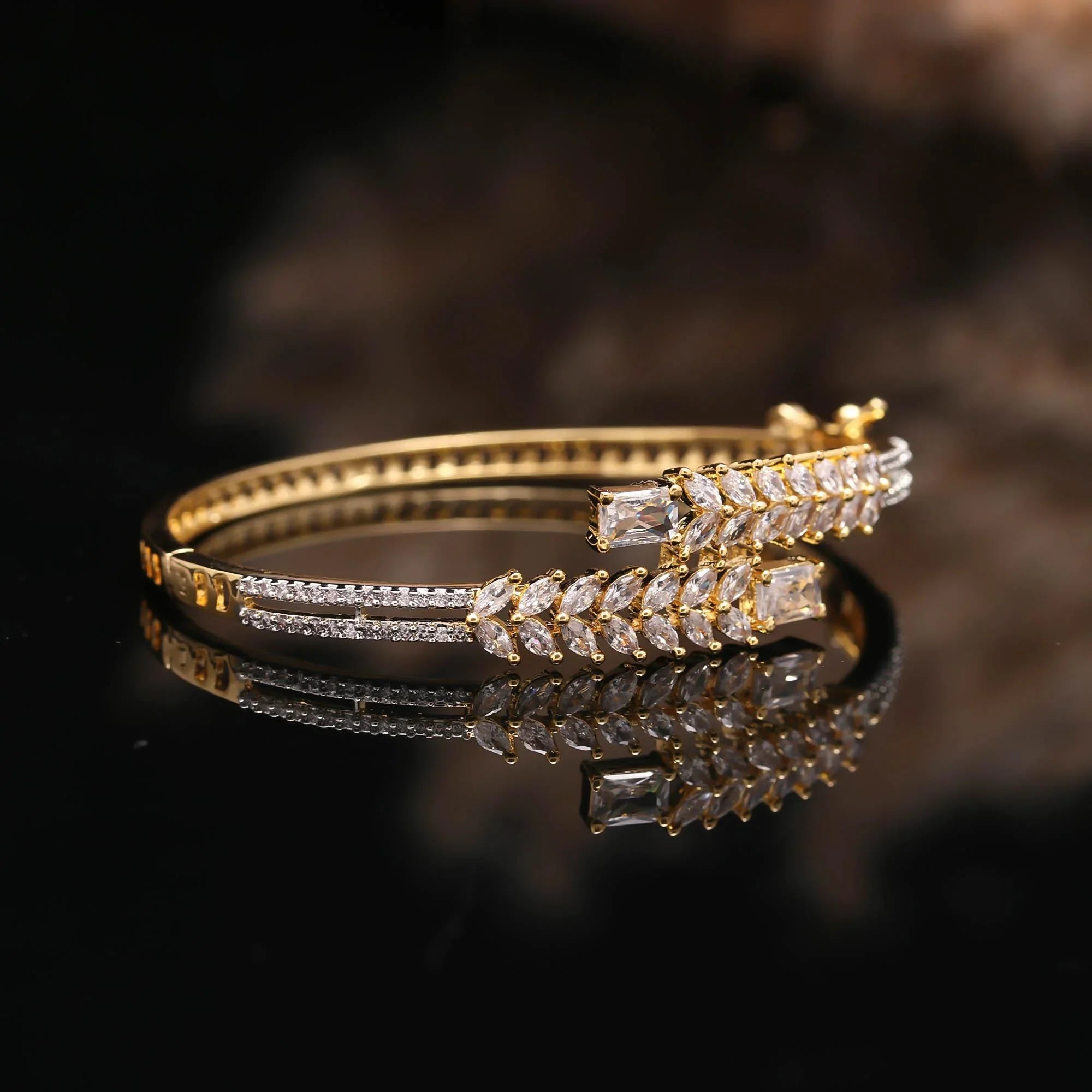 Elegant gold bracelet with diamond-shaped clear gemstones on black reflective surface by Haamsi