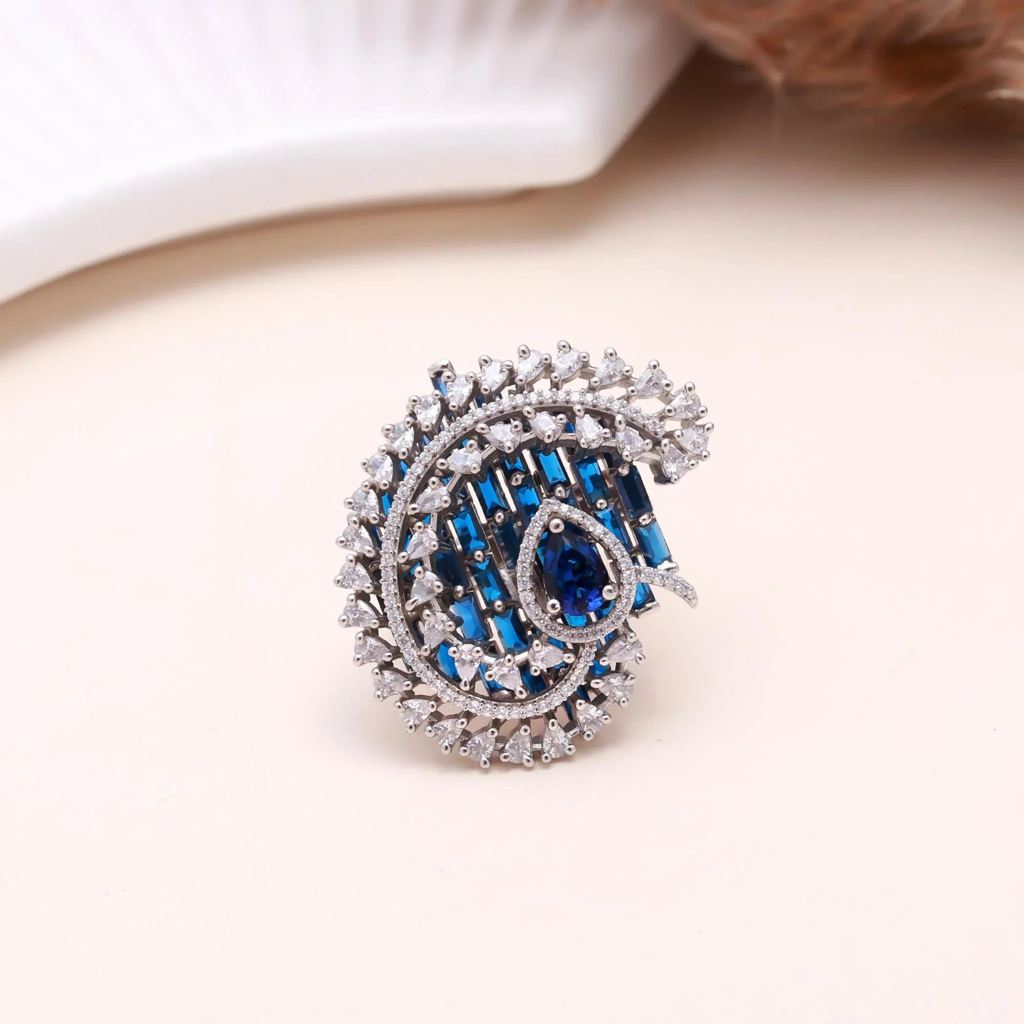Elegant silver ring with blue and clear gemstones in intricate swirl design on beige background