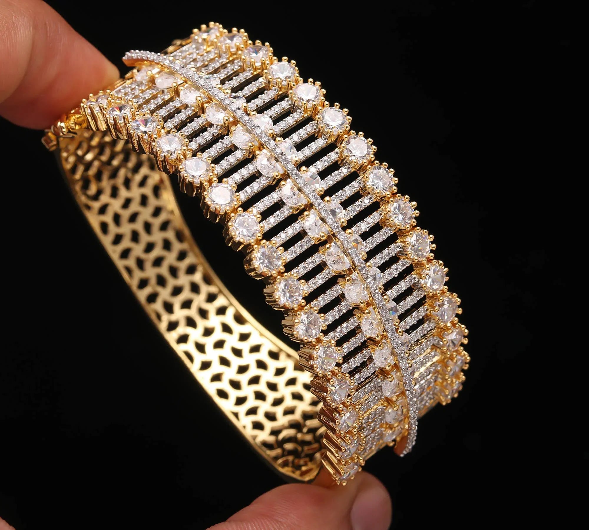 Hand holding luxurious gold bracelet with rows of round white gemstones and intricate lattice design