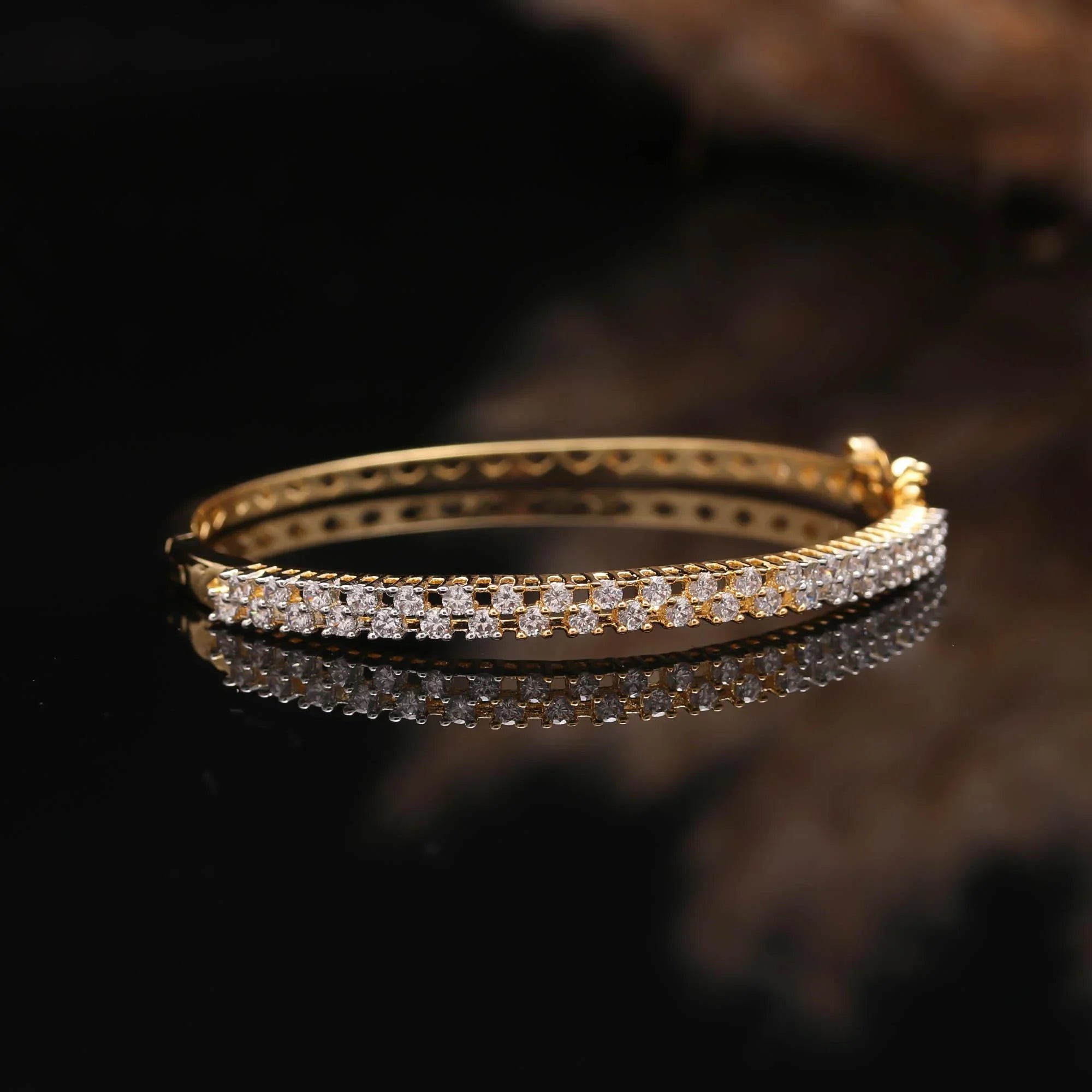 Elegant gold bangle bracelet with two rows of sparkling white gemstones on reflective black surface