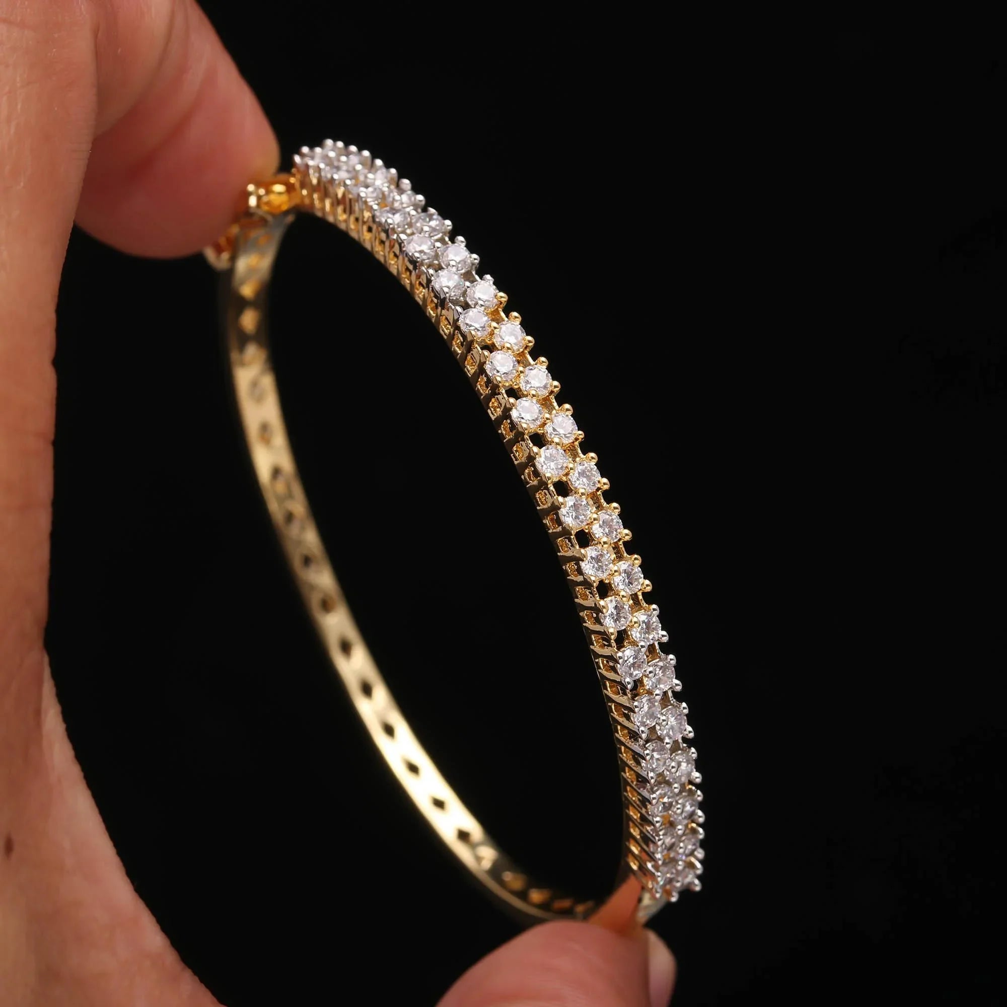Hand holding a gold bracelet with two rows of sparkling white gemstones on black background