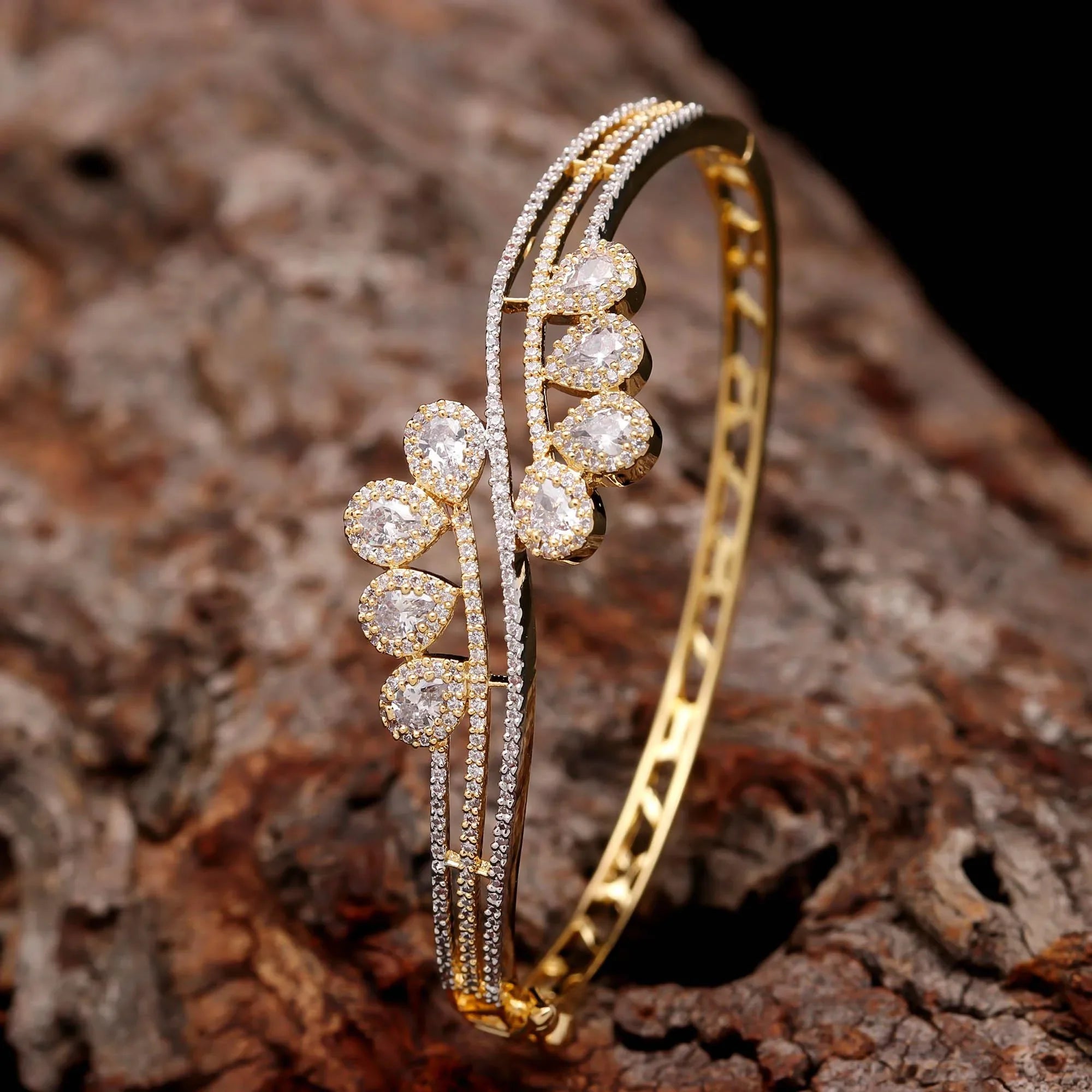 Gold-plated diamond bangle for women with teardrop-shaped stones on a textured wooden surface